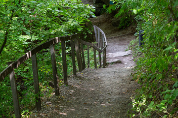 Long trail equipped with gravel steps and wooden handrail for tourists in sunny summer forest....