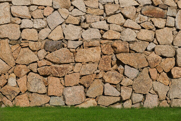 Chaotic beige stonework on a green lawn. Ancient historical masonry stone on the grass.
