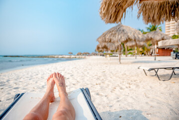 Woman's legs on sun lounger on white sandy beach