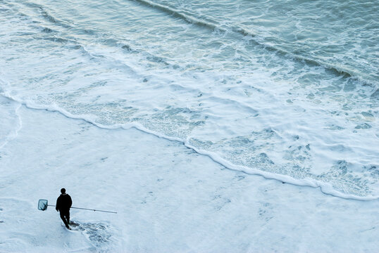 Lonely fisherman holding a fishnet walks on the beach.