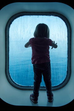 Girl looking through the glass of her cabin on her first boat trip, Grimaldi, Mediterranean Sea