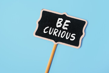 Be Curious - text on a small chalkboard on a blue background. Top view. Communication and brainstorming