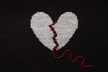 A broken heart is embroidered with white threads on black fabric.