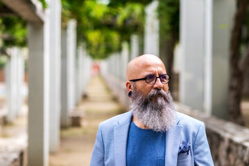 man posing standing with his hands in his pockets in a city park.