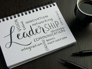 LEADERSHIP and related words handwritten in notepad with cup of espresso and pens on desk