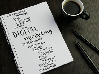 DIGITAL MARKETING word cloud in notebook with cup of coffee and pens on black wooden desk