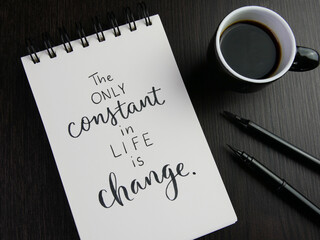 THE ONLY CONSTANT IN LIFE IS CHANGE lettering in notebook with cup of coffee and pens on black...