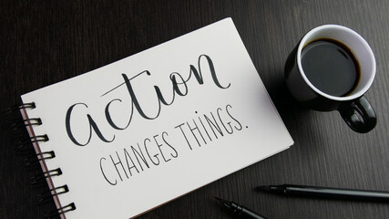 ACTION CHANGES THINGS. lettering in notebook with cup of coffee and pens on black wooden desk