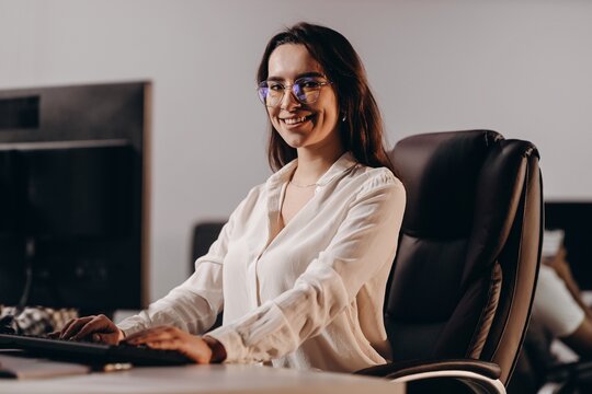 Smiling girl in glasses working in office. Beautiful receptionist woman typing on computer keyboard