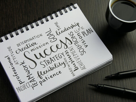 SUCCESS word cloud handwritten in notebook with cup of coffee and pens on black wooden desk