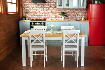 Interior design scandinavian kitchen with utensils and furniture. Stylish dining room with table and chair. Cuisine with vase with flowers on table. Facade of wooden blue kitchen with red refrigerator