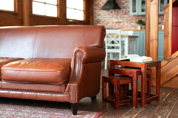 Modern design of room in loft style.Fragment of the interior of a country house. Comfortable Brown eco leather couch standing in living room with modern interior design and wooden coffee table.	