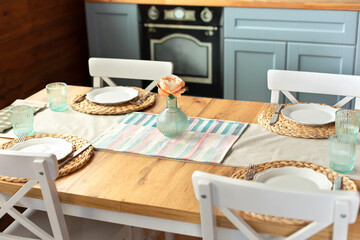 Table setting for dinner at home. Beautiful served table with runner on table, vase with flowers and plates in living room. Stylish dining room with table and wooden chairs. Cozy kitchen with dishes.	