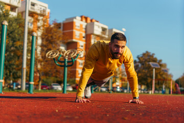 Male athlete exercising in the park doing push-ups and focused on working on his upper body