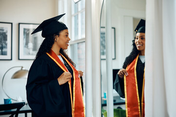 Happy black graduate student looking herself in mirror while getting ready for the ceremony.