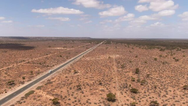 Aerial drone panning shot of a camper van on empty road in barren environment on a sunny day. Nullarbor, Australia