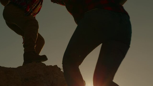 Silhouette woman lends helping hand to companion while climbing to top of mountain in travel.