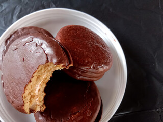 A chocolate-covered cake with a marshmallow filling in the center, served on a small white plate with a crumpled black background.