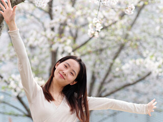 Outdoor portrait of beautiful young Chinese girl posing with blossom white cherry flowers background in spring garden, beauty, summer, emotion, lifestyle, expression and people concept.