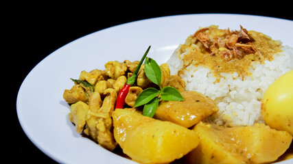 Side Angle of Chicken curry rice in yellow spice sauce with potatoes and boiled egg served on white plate isolated on black dark background