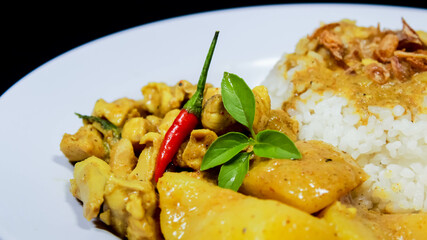 Side Angle of Chicken curry rice in yellow spice sauce with potatoes and boiled egg served on white plate isolated on black dark background