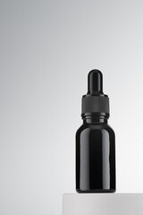 A dark glass bottle with a pipette containing a cosmetic product. Gray background.Copy space.
