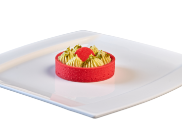 Sweet dessert: Tarts, Tartlets. A bright red basket of shortbread dough and a delicate green pistachio filling. Close-up on a white plate