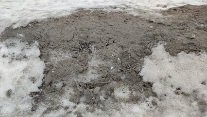 White-black melting snow. On a winter day, the dirty white snow began to melt, revealing debris, dust, and dirt stuck in it. Snow loose once was white now has a dark gray