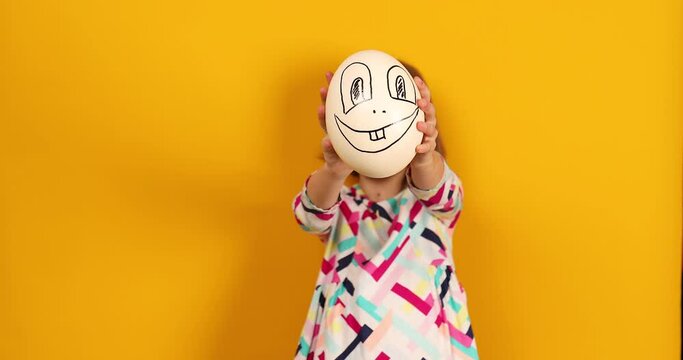 Playful teenager girl covering her face of Ostrich egg with funny face on a bright yellow studio background, Face on the egg, celebrating Easter in style.
