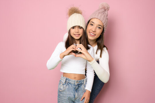 Portrait of two nice cute lovable winsome tender lovely attractive charming cheerful positive straight-haired girls showing heart shape isolated over pink background