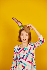 Happy playful teenager girl wearing bunny ears on a bright yellow studio background, celebrating Easter in style.