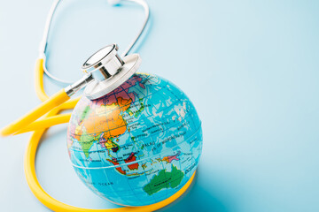 World Health Day. Top view yellow doctor stethoscope wrapped around world globe isolated on pastel...
