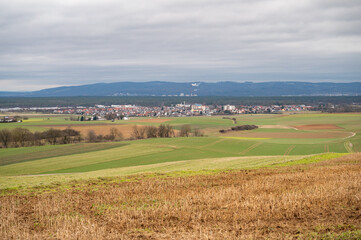 Fototapeta na wymiar Cityscape of Schaafheim, with agricultural fields in the front and Mountain range in the background during cloudy day, Germany