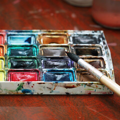 Watercolor paints and a brush on the table. Selective focus