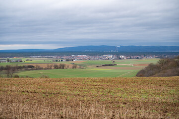 Fototapeta na wymiar Cityscape of Schaafheim and village next to it, with agricultural fields in the front and Mountain range in the background during cloudy day, Germany