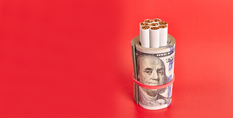 Cigarettes wrapped in 100 dollar bills on a red background. Concept of expensive cigarettes.