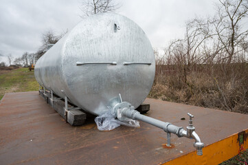 Silver Metal water tank with water pump in front on a trailer outdoors next to an agricultural field