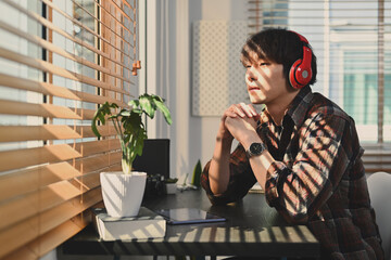 Pleased man looking through window while listening to music, podcast or audio book on wireless headphone
