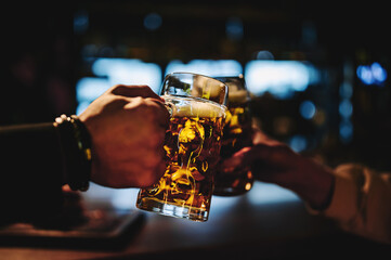 man and woman hands clinking glasses of light beer at the pub or bar