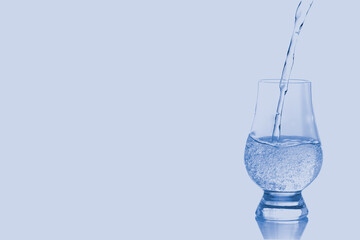 Pure water pouring into glass isolated on blue background.