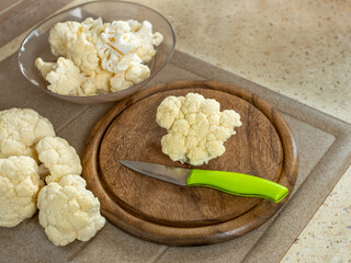 Fresh cauliflower, a wooden cutting board and a knife on the kitchen table. Flat layout. Place for...