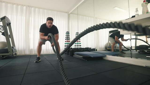 Young man Using Battle Ropes For fast pacing Whipping Exercise in a Gym