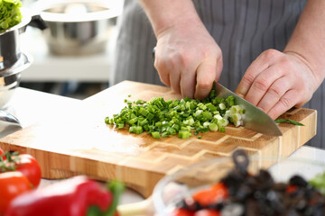 ook cuts green onions on board in kitchen