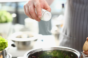Chef adds salt from salt bowl to dish closeup