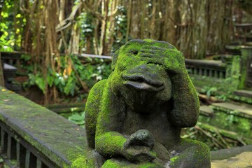 Close-up of a moss-covered stone figure in the shape of a frog in the middle of a sun-drenched rainforest, with a temple complex diffused in the background.