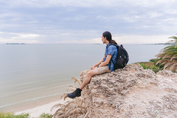 Young latin man sitting on a rock belonging to a cliff with the ocean in the background. Copy space.