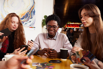 A bunch of young people, girls and guys in a cafe, talking, having fun, taking selfies, chatting on phones.