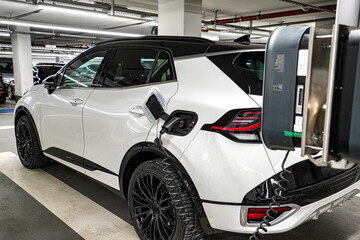 A white electric car is charging in an underground parking lot. The concept of ecological energy systems.