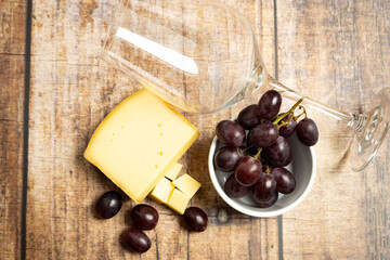 top view of red grapes with cheese and a wineglass on a wooden background