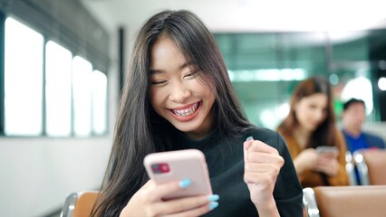 Happy Asian woman using phone celebrating success online win, girl reading good news, in gate at...